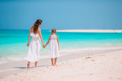 Rear view of mother and daughter holding hand on beach