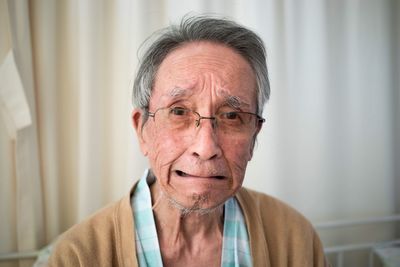 Portrait of senior man crying while sitting against curtain at home