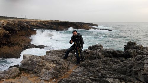 Man standing on rock by sea against sky