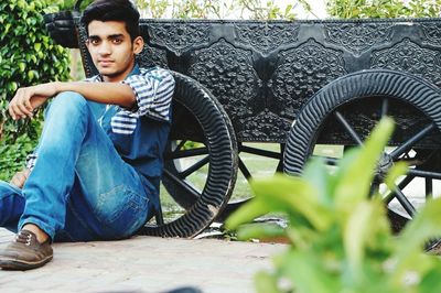 Portrait of young man sitting by cart at park