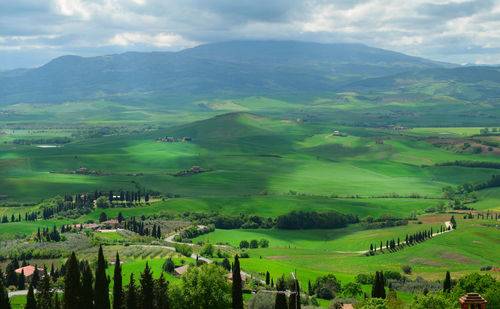 High angle view of green landscape and mountains against cloudy sky