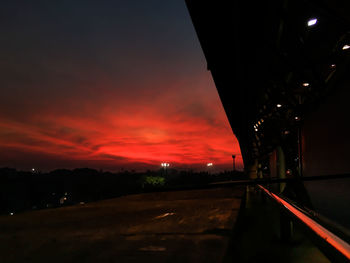 Road by silhouette city against orange sky