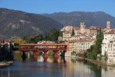 Bridge over river by buildings in city against sky