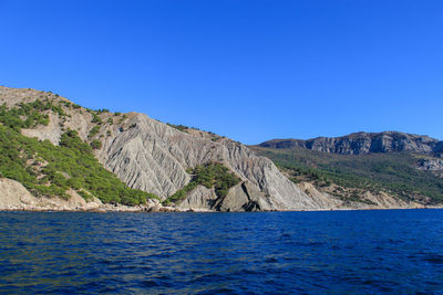 Scenic view of sea and mountains against clear blue sky