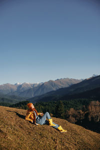 Rear view of man sitting on mountain against clear sky