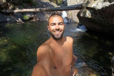 Portrait of smiling shirtless man standing on stream in forest