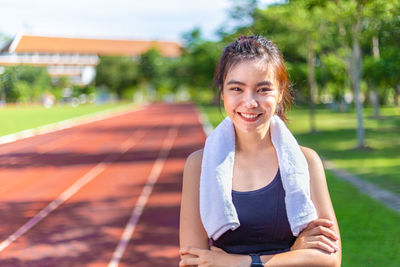 Happy beautiful young asian woman exercise in the morning at running track standing cross arms smile