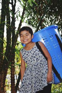 Portrait of smiling girl carrying basket on back against trees