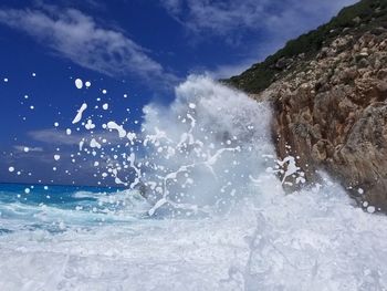 Water splashing on rocks against sky