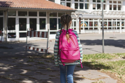 A girl with a pink satchel on her back approaches the school door. the first day of school.