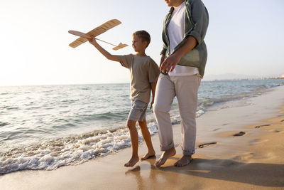 Father and son launching handmade wooden plane on the beach at sunset