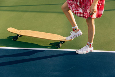 Girl in dress with foot on skateboard on a tennis court