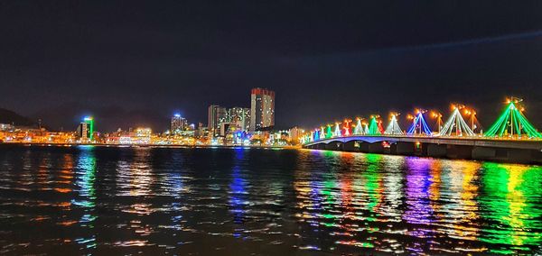 Illuminated buildings by river against sky at night