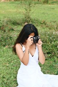 Young woman drinking water while sitting on grassy field