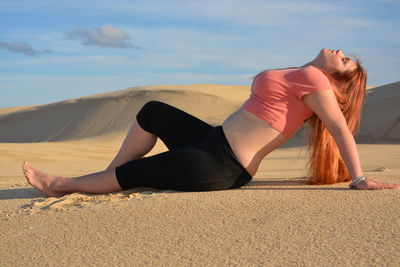 Full length young woman lying on sand at desert