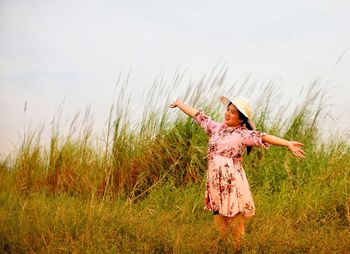 Woman with arms outstretched standing on field against sky