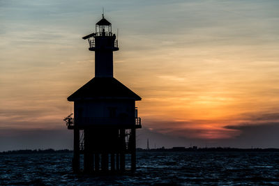 Lighthouse by sea against sky during sunset