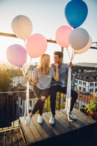 Young woman and man with balloons against sky in city