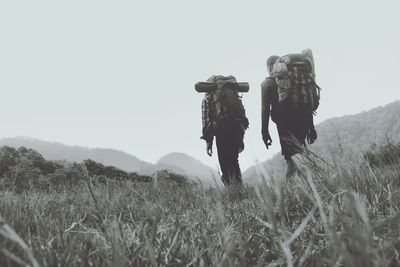 Rear view of people walking on field against clear sky