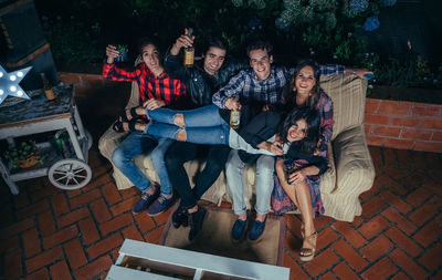 High angle view of cheerful friends on sofa at patio during night