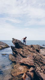 Shirtless man standing on rock at beach against cloudy sky