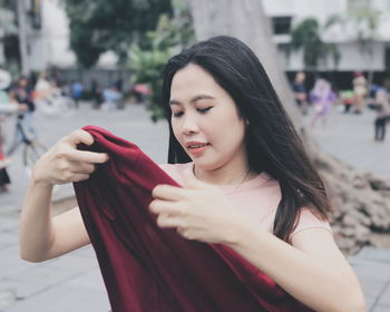 Young woman holding jacket while standing on footpath in city