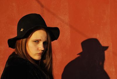 Portrait of young woman wearing hat by wall
