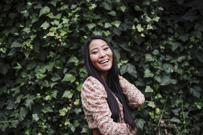 Portrait of a smiling young woman standing against plants