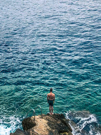 High angle view of man standing on rock by sea