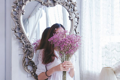 Midsection of woman holding flowering plants by window