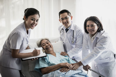 Portrait of senior woman lying on bed with doctors standing at hospital