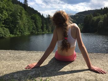 Rear view of woman sitting on retaining wall against lake