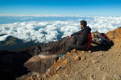 Man sitting on rock looking at mountains against sky