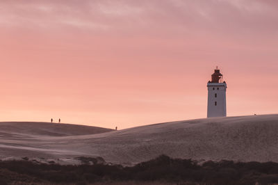 Lighthouse on beach against sky during sunset