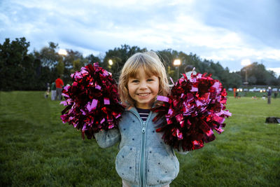 Little girl smiling with pom poms outside at dusk