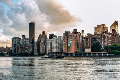 Modern buildings by river against sky in city
