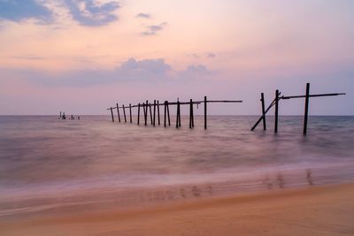 Wooden posts on beach against sky during sunset