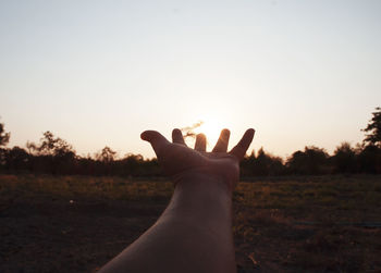 Midsection of person hand on field against sky during sunset