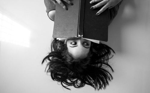 High angle view of woman covering face with book while lying on floor