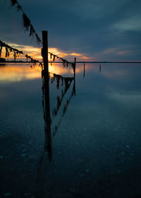 Silhouette wooden post on sea against sky at sunset