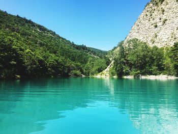Scenic view of lake by trees against clear blue sky