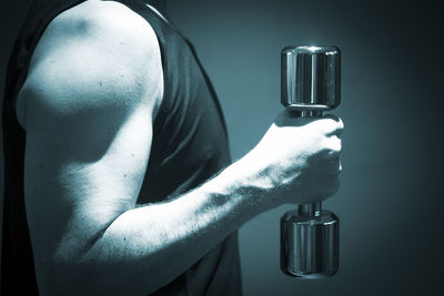 Midsection of man lifting dumbbell