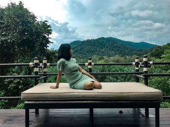 Woman sitting on railing against mountain