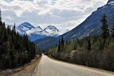 Road amidst trees and snowcapped mountains against sky