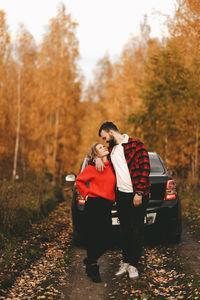 A romantic couple in love in warm sweaters is walking traveling by car in the autumn forest in fall