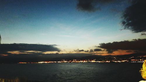 Illuminated city by sea against sky at sunset