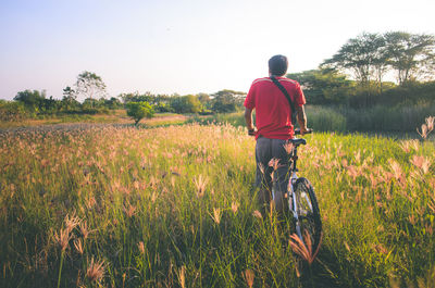 Rear view of man cycling on field against sky