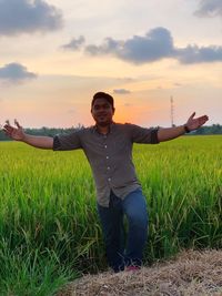 Man with arms raised on field against sky during sunset