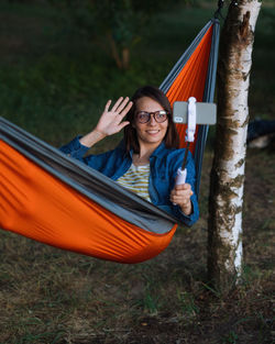  female travel blogger is sitting in a hammock recording videos on her phone. social media content