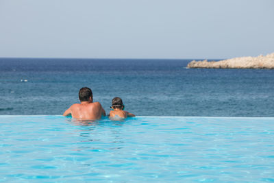 Rear view of shirtless man in swimming pool against sea